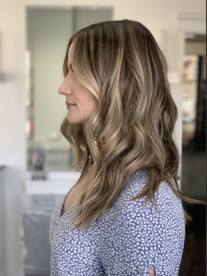 Side view of a woman with wavy, highlighted hair in a salon.