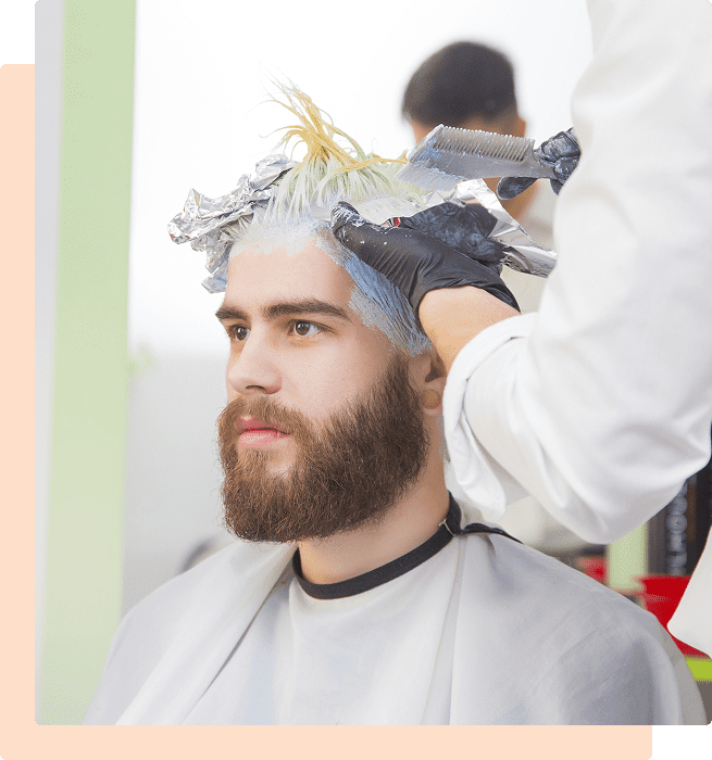 A man getting his hair dyed in a salon with gloves on the stylist.