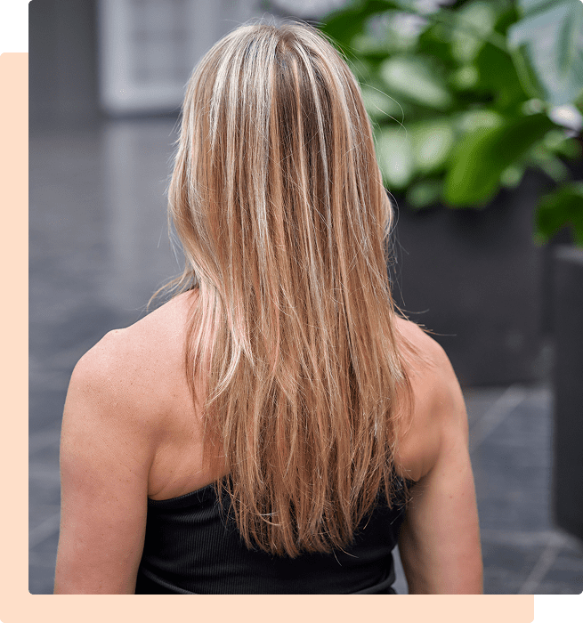 Woman with long blonde hair wearing a black top, photographed from behind.