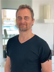 Man smiling, wearing a black t-shirt indoors.