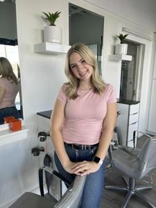 A woman with blonde hair smiles in a modern indoor setting.