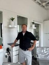 Man standing in a modern kitchen with a dog beside him.